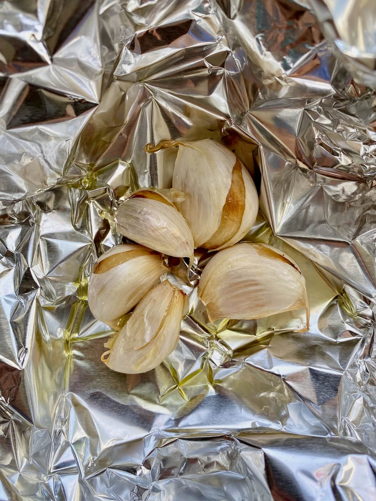 Five cloves of roasted garlic in aluminum foil.