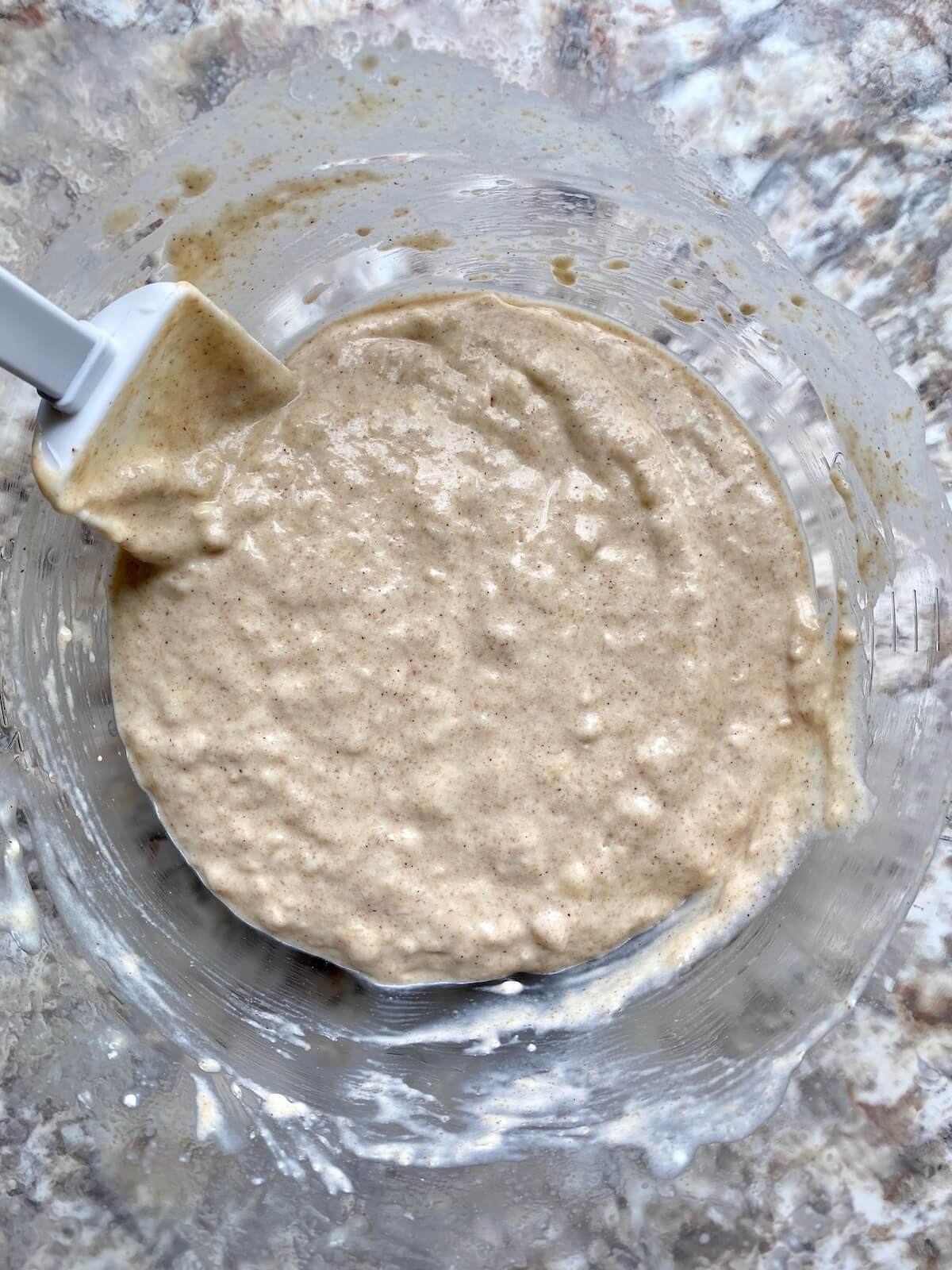 Sourdough banana pancake batter in a glass bowl with a rubber spatula sticking out to the left.