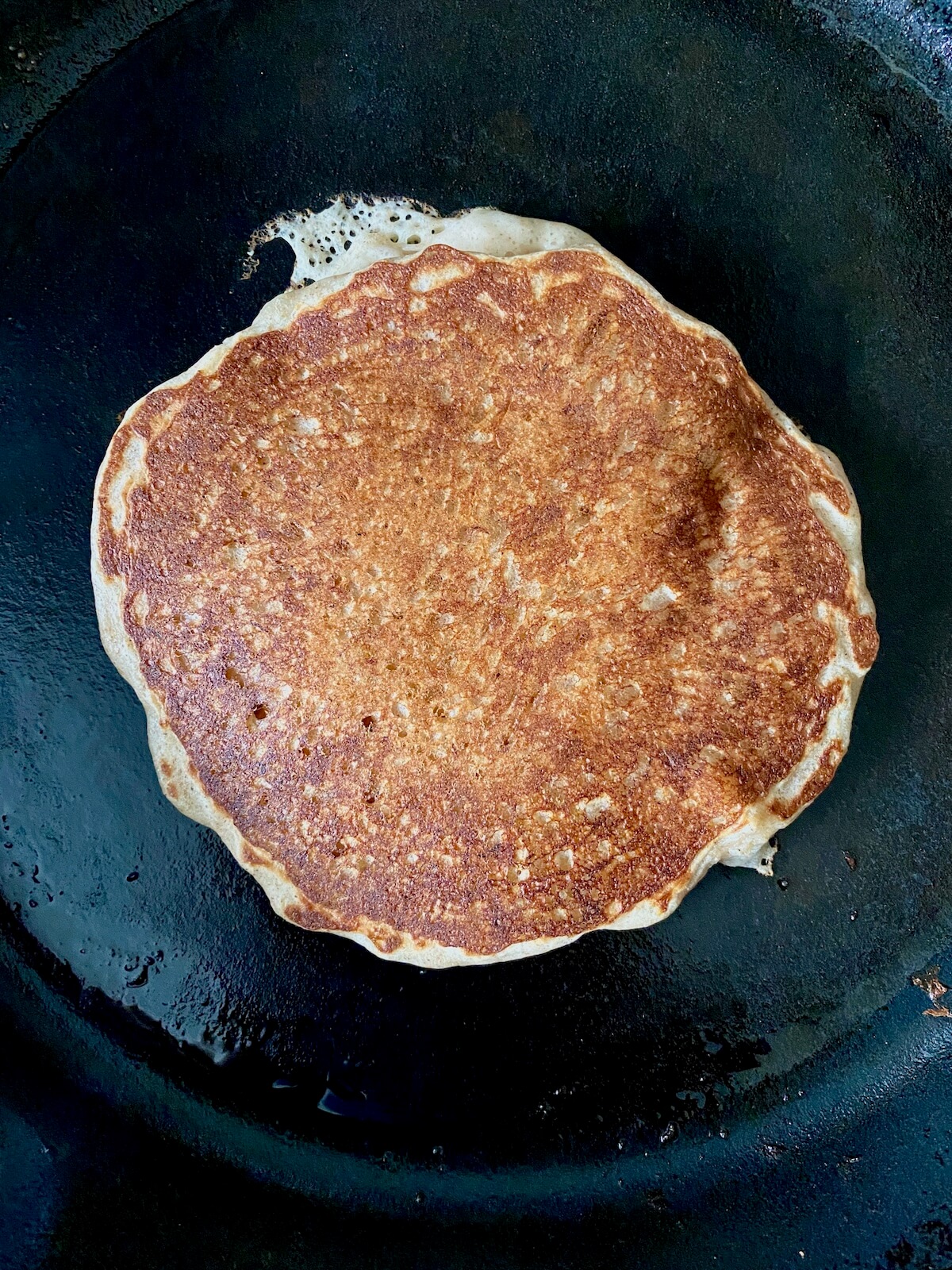 A cooked sourdough banana pancake in a cast iron skillet.
