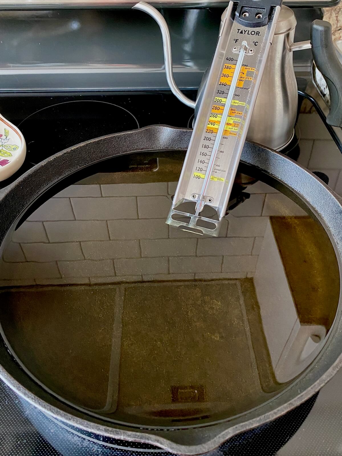 A large cast iron skillet filled with oil on a stovetop with a thermometer sticking out.