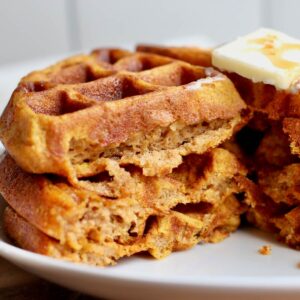 Sourdough pumpkin waffles on a plate topped with butter and maple syrup.