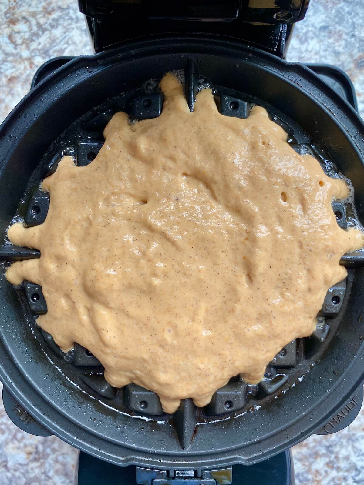 Pumpkin sourdough waffle batter in a waffle maker.