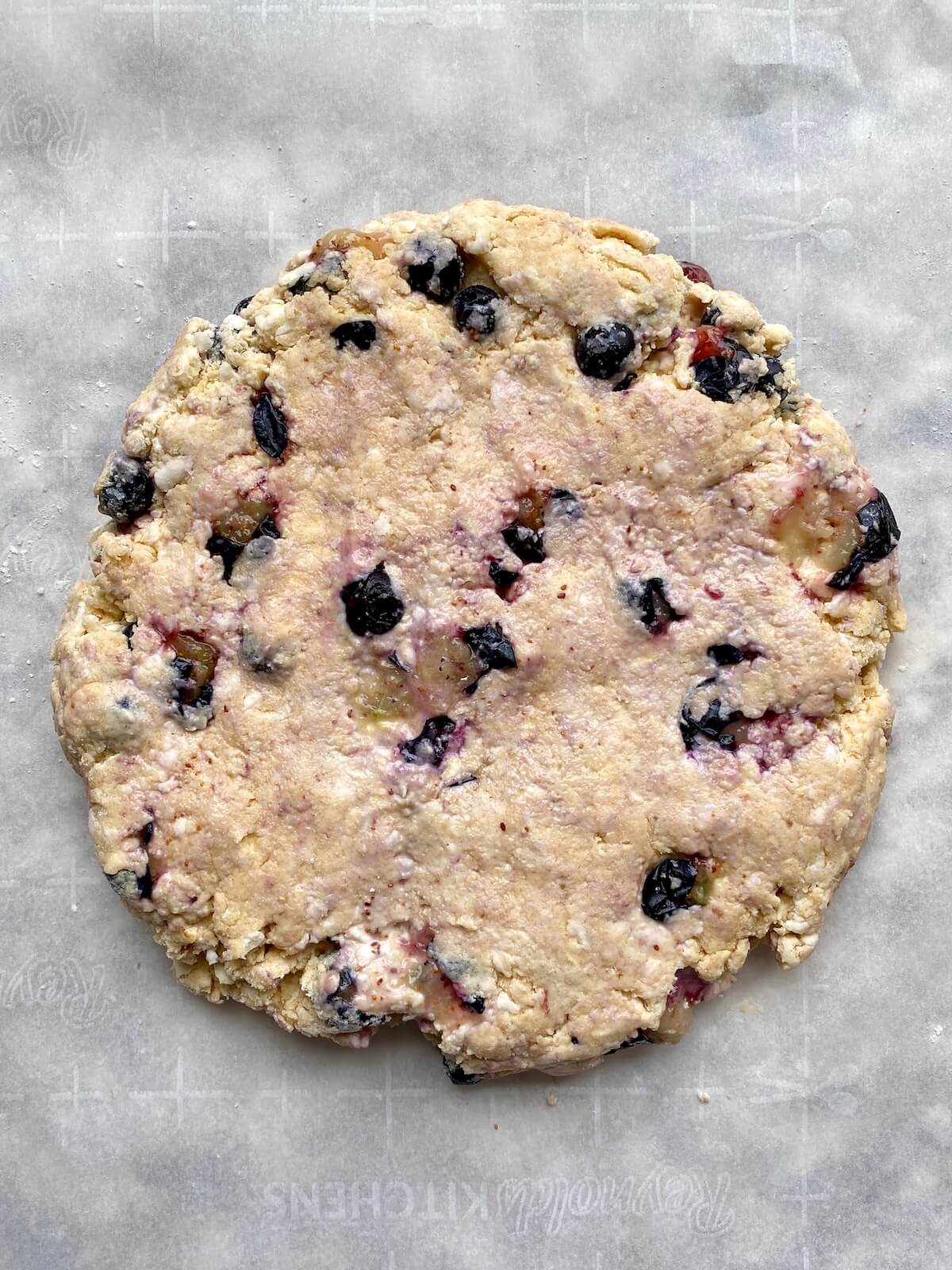 Blueberry sourdough scone dough formed into a disc on a parchment-lined baking sheet.