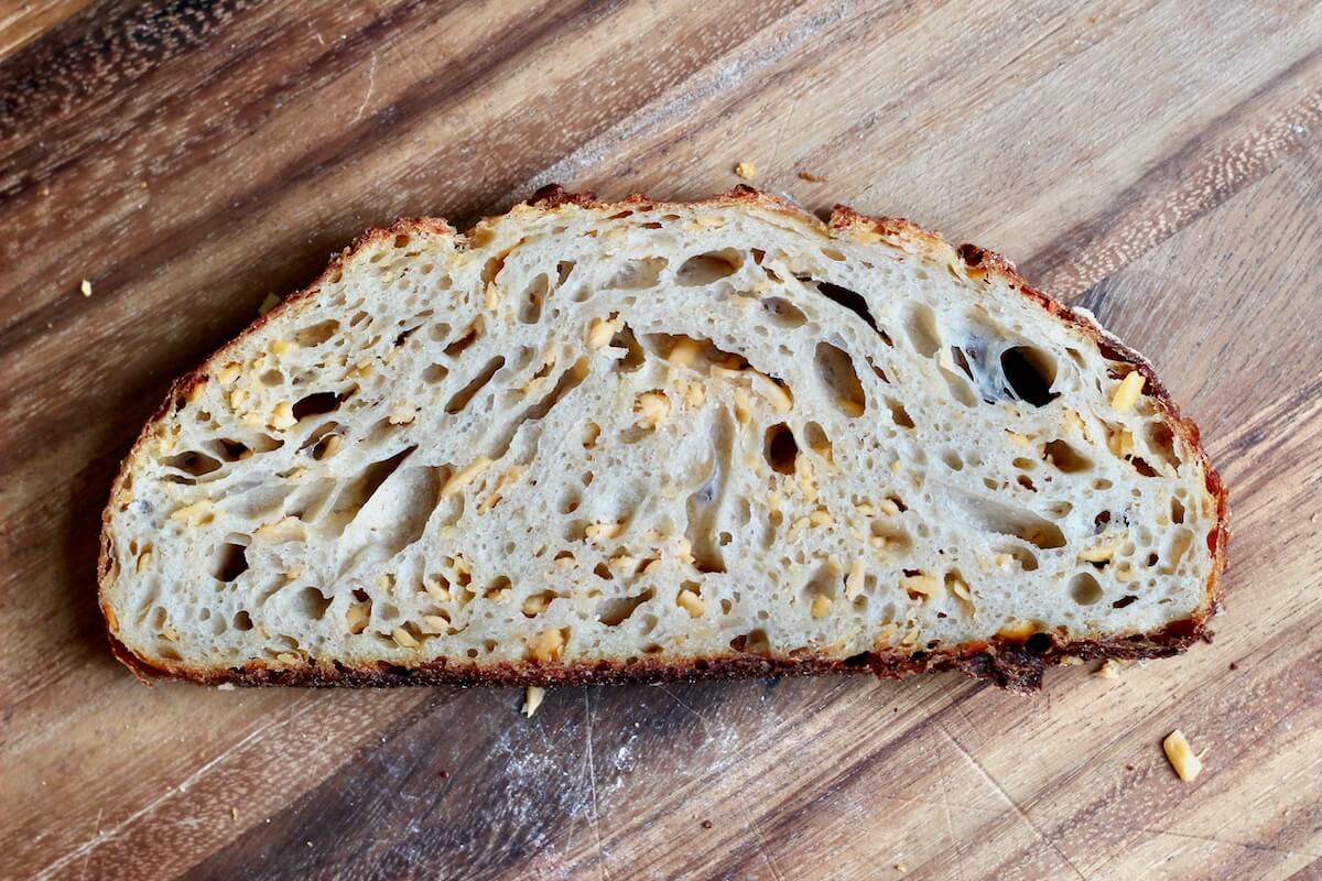 A slice of cheddar cheese sourdough bread on a wooden cutting board.
