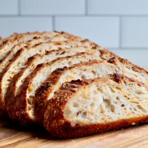A loaf of cheddar cheese sourdough bread sliced on a wooden cutting board.