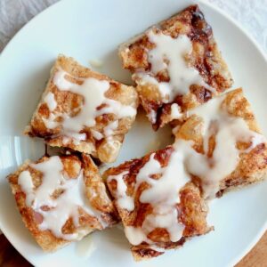 Five pieces of sourdough discard cinnamon roll focaccia with icing on a small white plate.