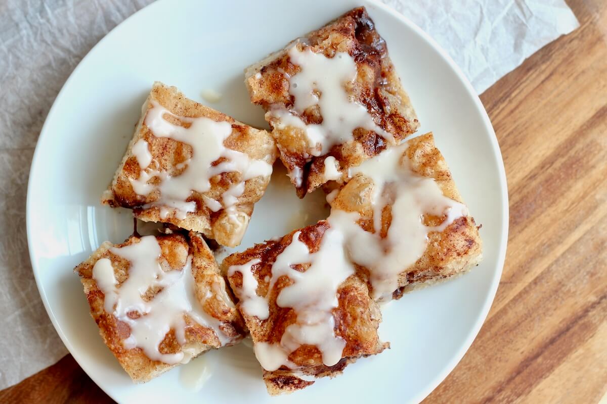 Five pieces of sourdough discard cinnamon roll focaccia with icing on a small white plate.