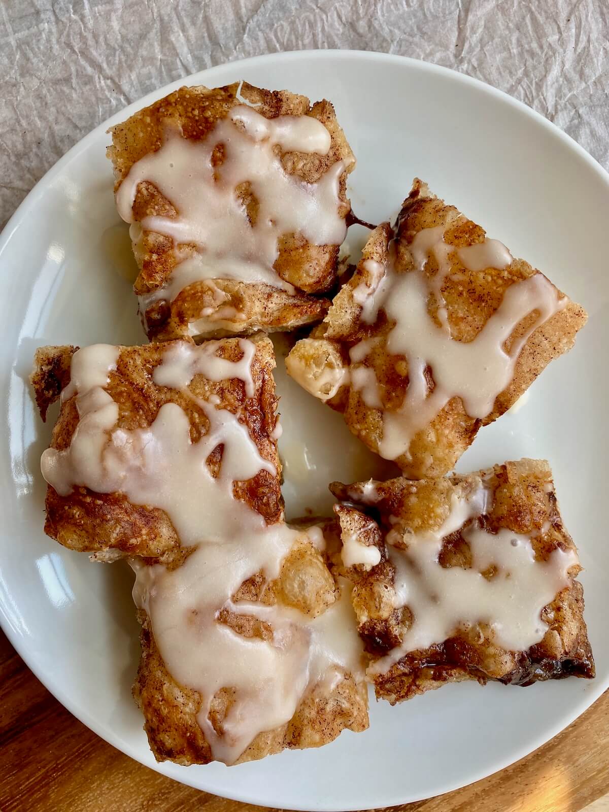 Five pieces of sourdough discard cinnamon roll focaccia with icing on a small white plate.
