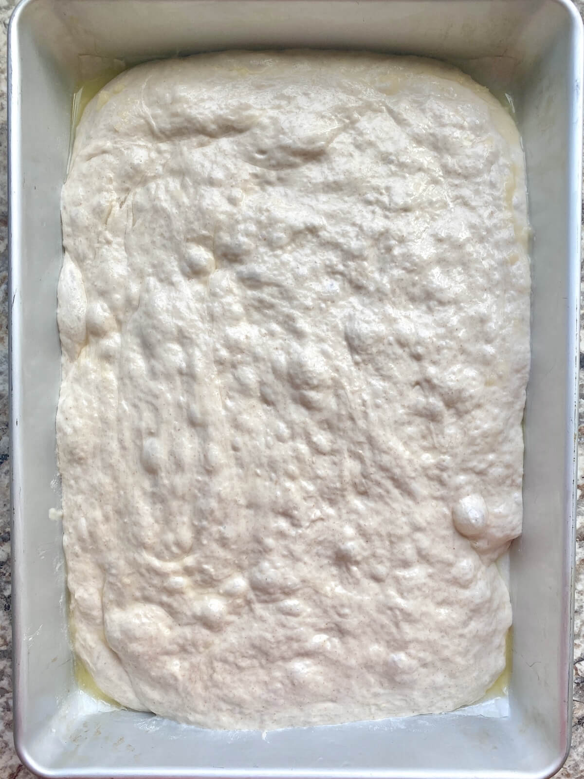 Sourdough focaccia dough in an aluminum baking pan before proofing.