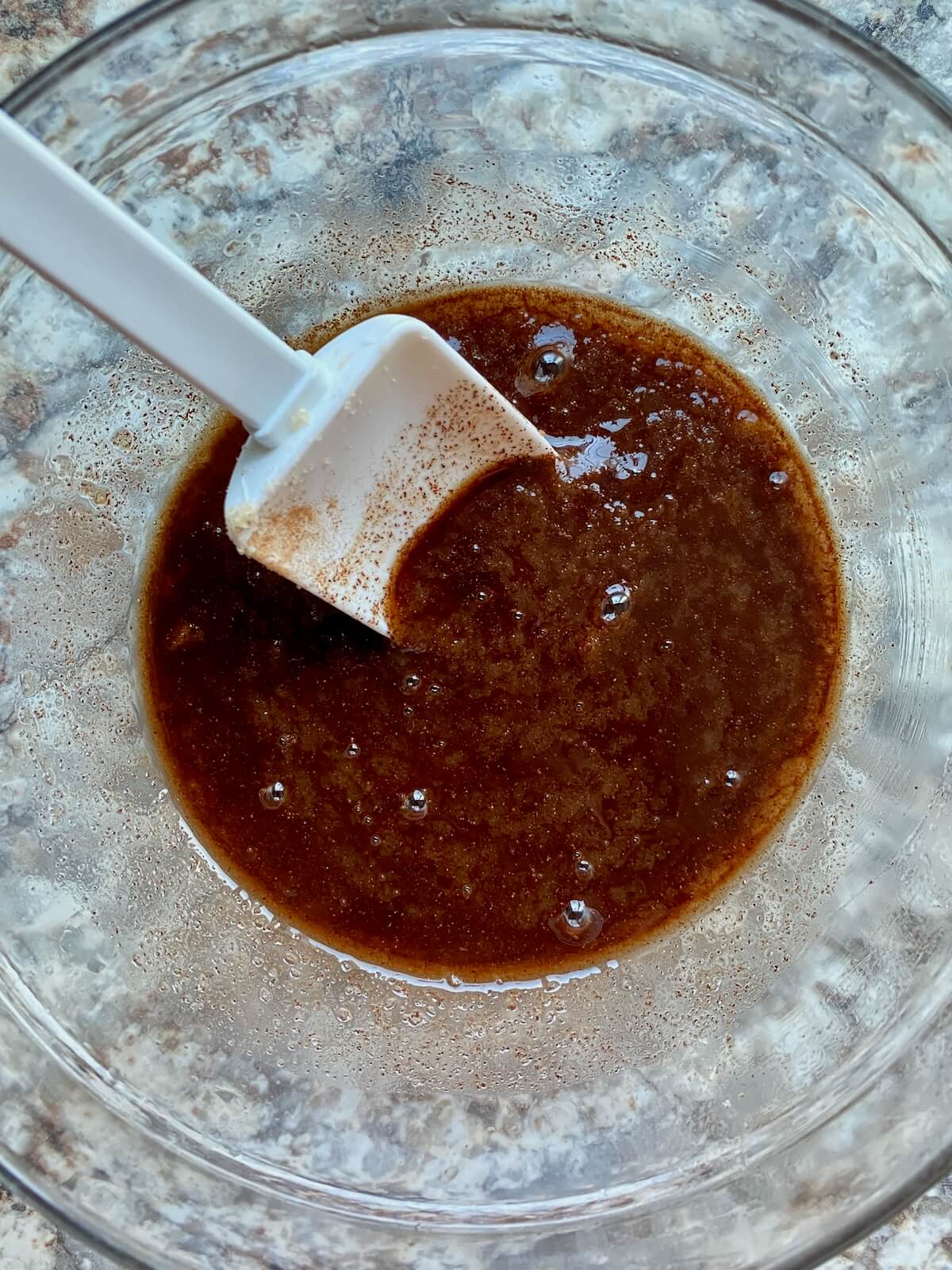 Cinnamon sugar filling mixed together in a small glass bowl with a white rubber spatula sticking out to the left.