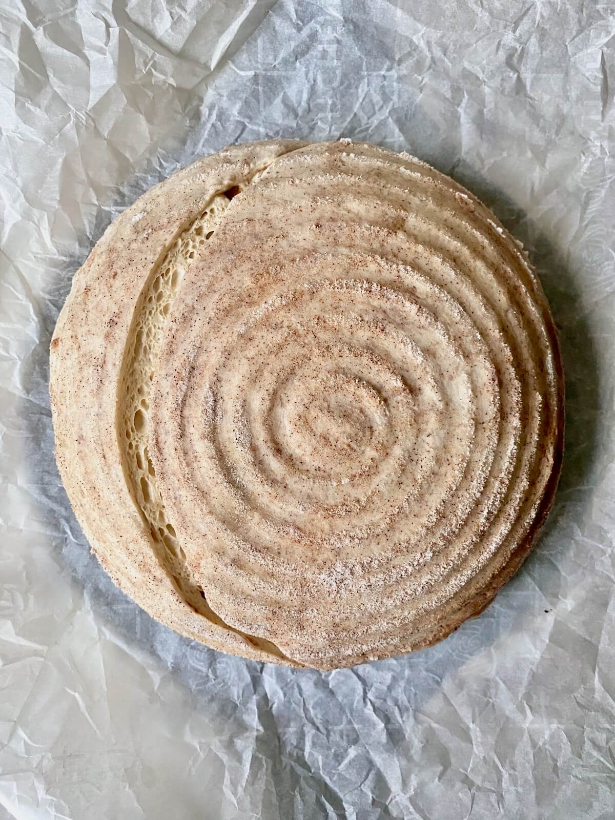 A scored loaf of cinnamon sugar sourdough bread on a piece of parchment paper.