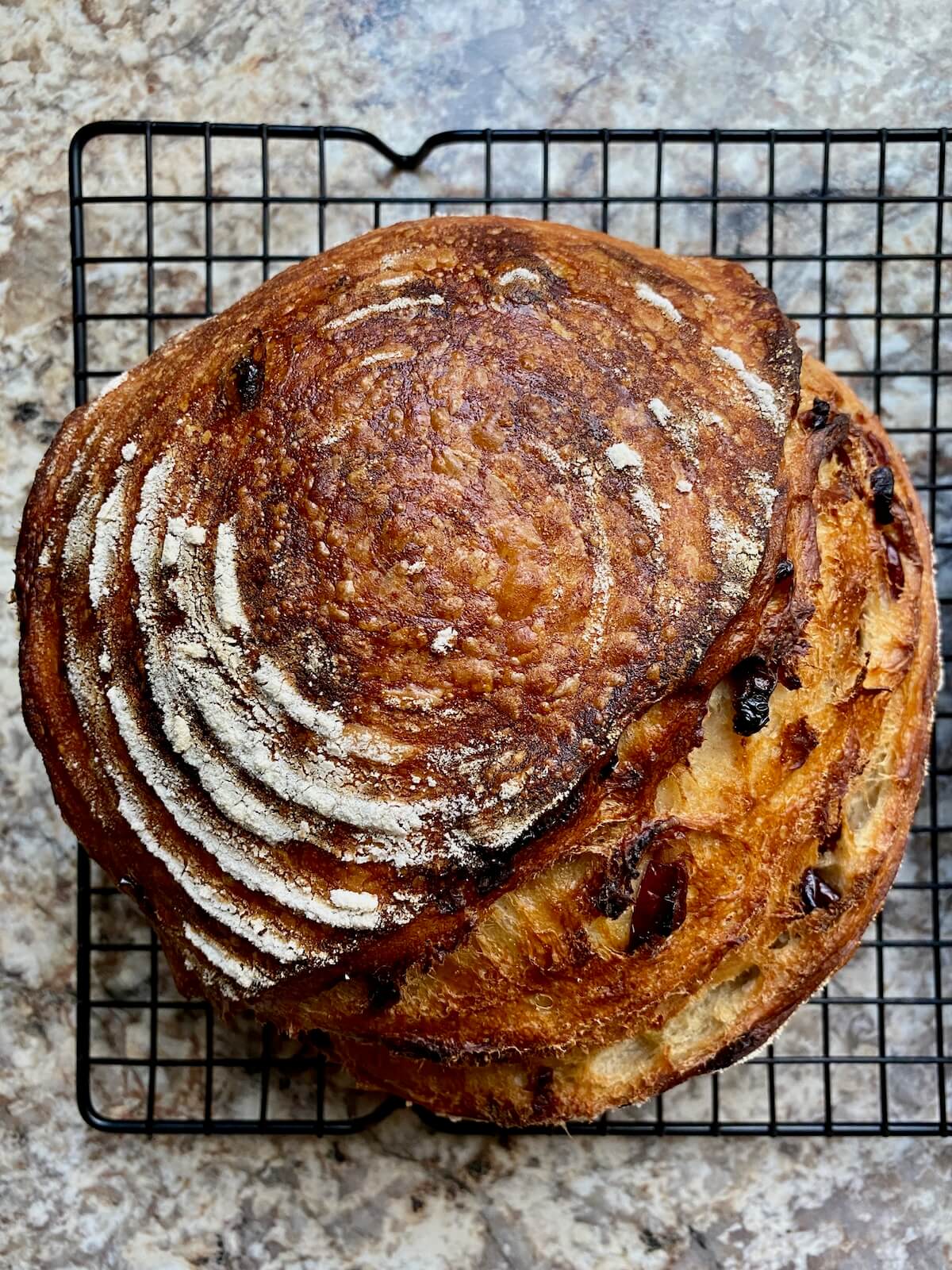 A baked loaf of cranberry orange sourdough bread on a wire cooling rack.