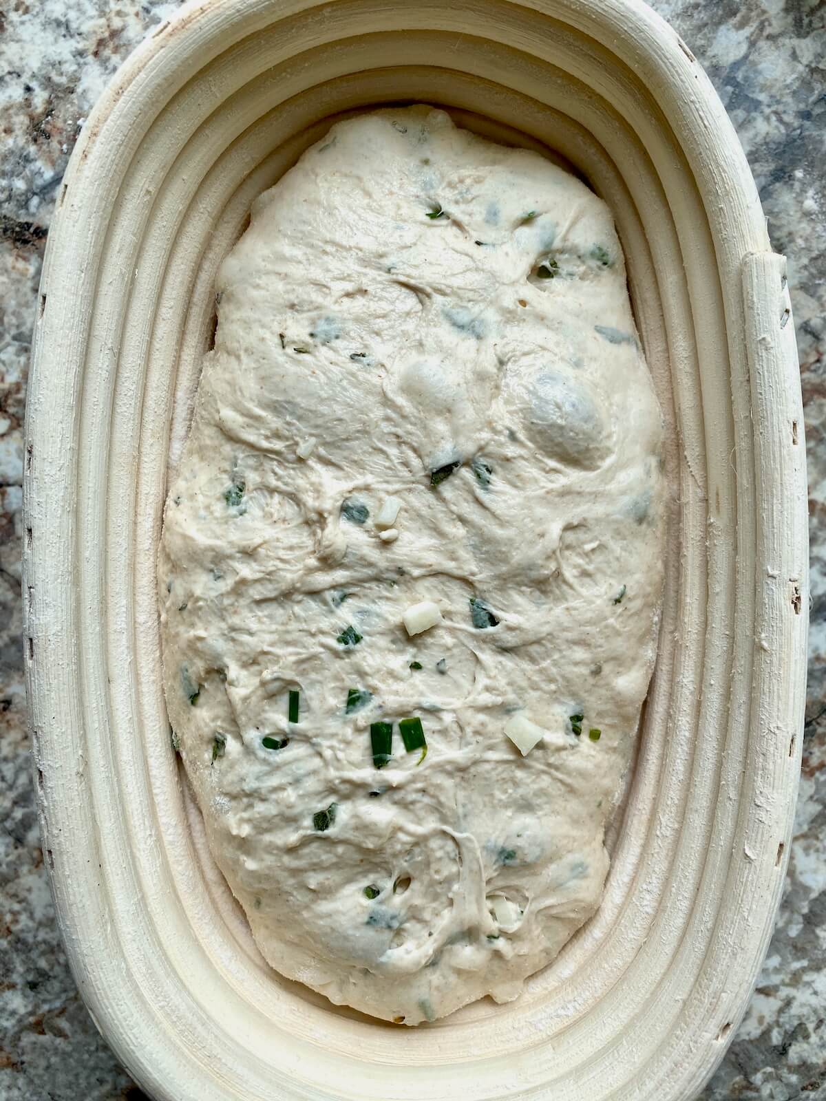 Garlic sourdough bread dough in an oval proofing basket.