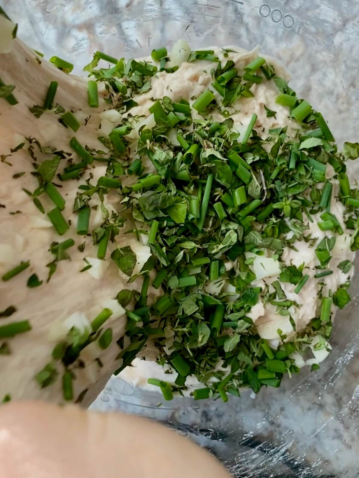 Garlic herb sourdough bread dough being stretched and folded in a bowl.