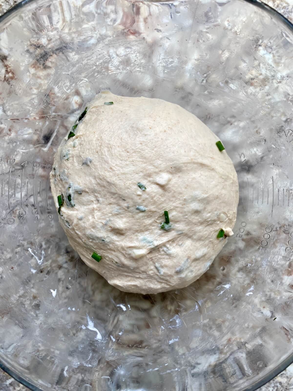 A stretched and folded sourdough bread dough ball in a glass bowl.