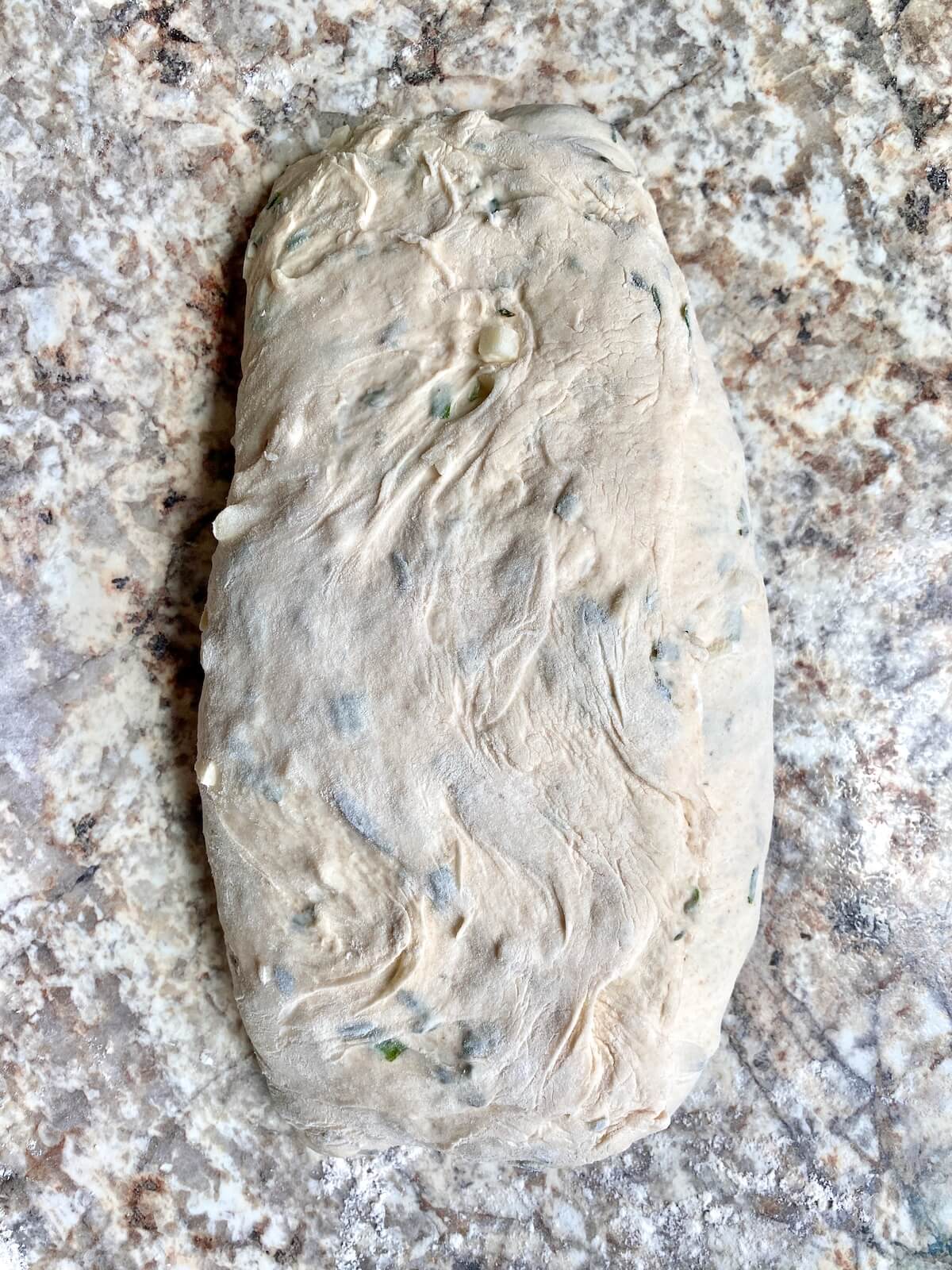 Garlic sourdough bread dough folded into thirds while being shaped.