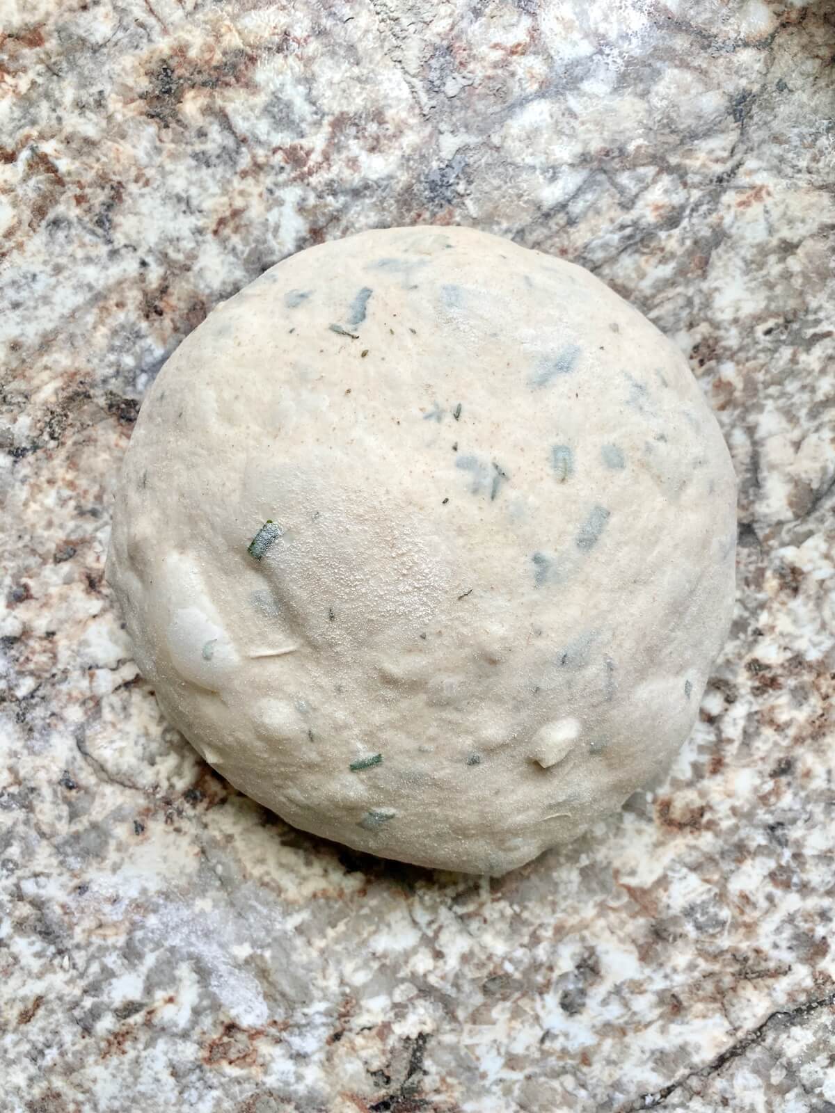 A garlic herb sourdough bread dough ball on a counter.