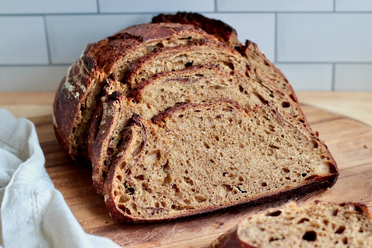 A loaf of gingerbread sourdough bread cut into slices on a cutting board.