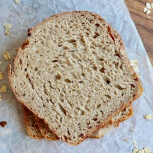 Slices of oatmeal sourdough bread stacked on top of a piece of parchment paper.