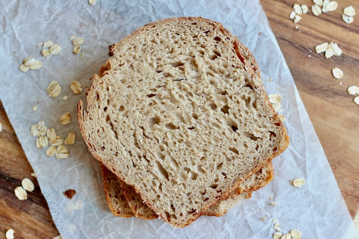 Slices of oatmeal sourdough bread stacked on top of a piece of parchment paper.