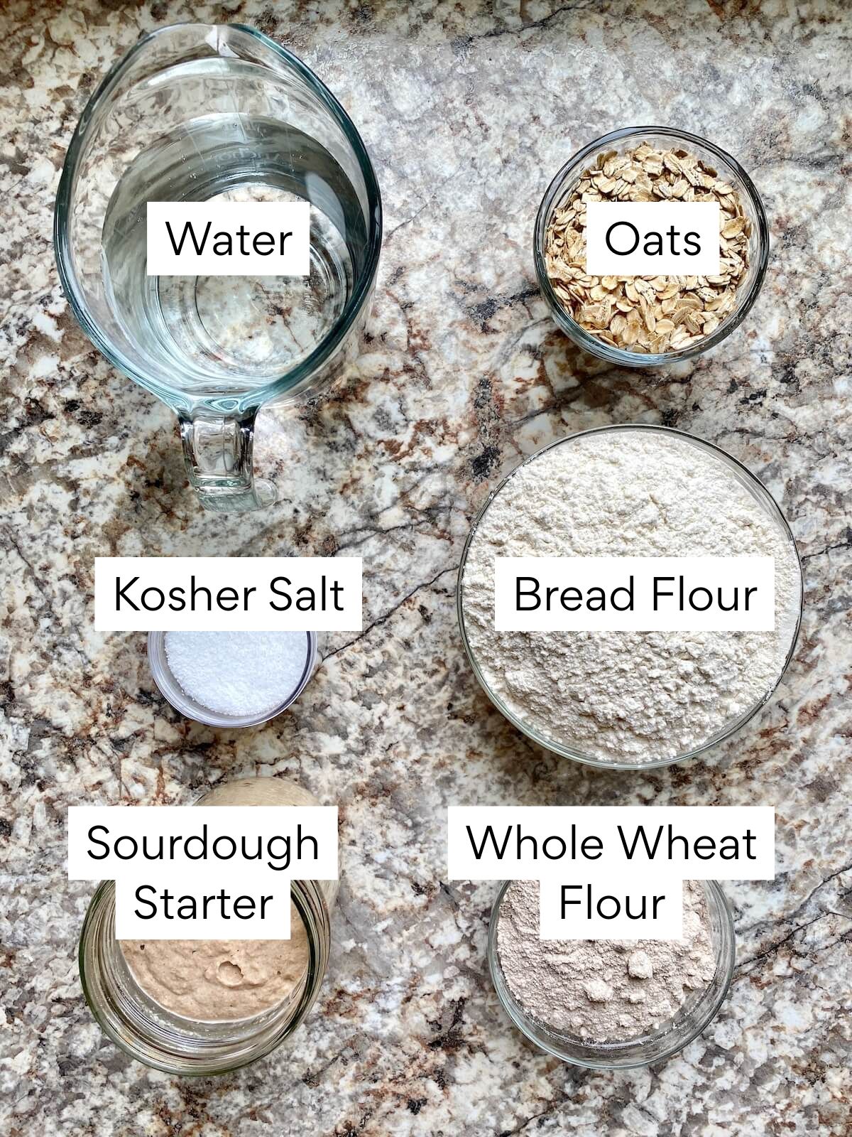 The ingredients to make oatmeal sourdough bread. Each ingredient is labeled with text. They include water, oats, bread flour, kosher salt, sourdough starter, and whole wheat flour.