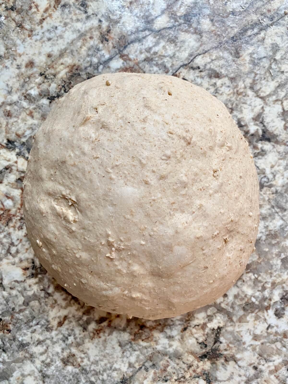 The oatmeal sourdough bread dough shaped into a round ball on a floured counter.