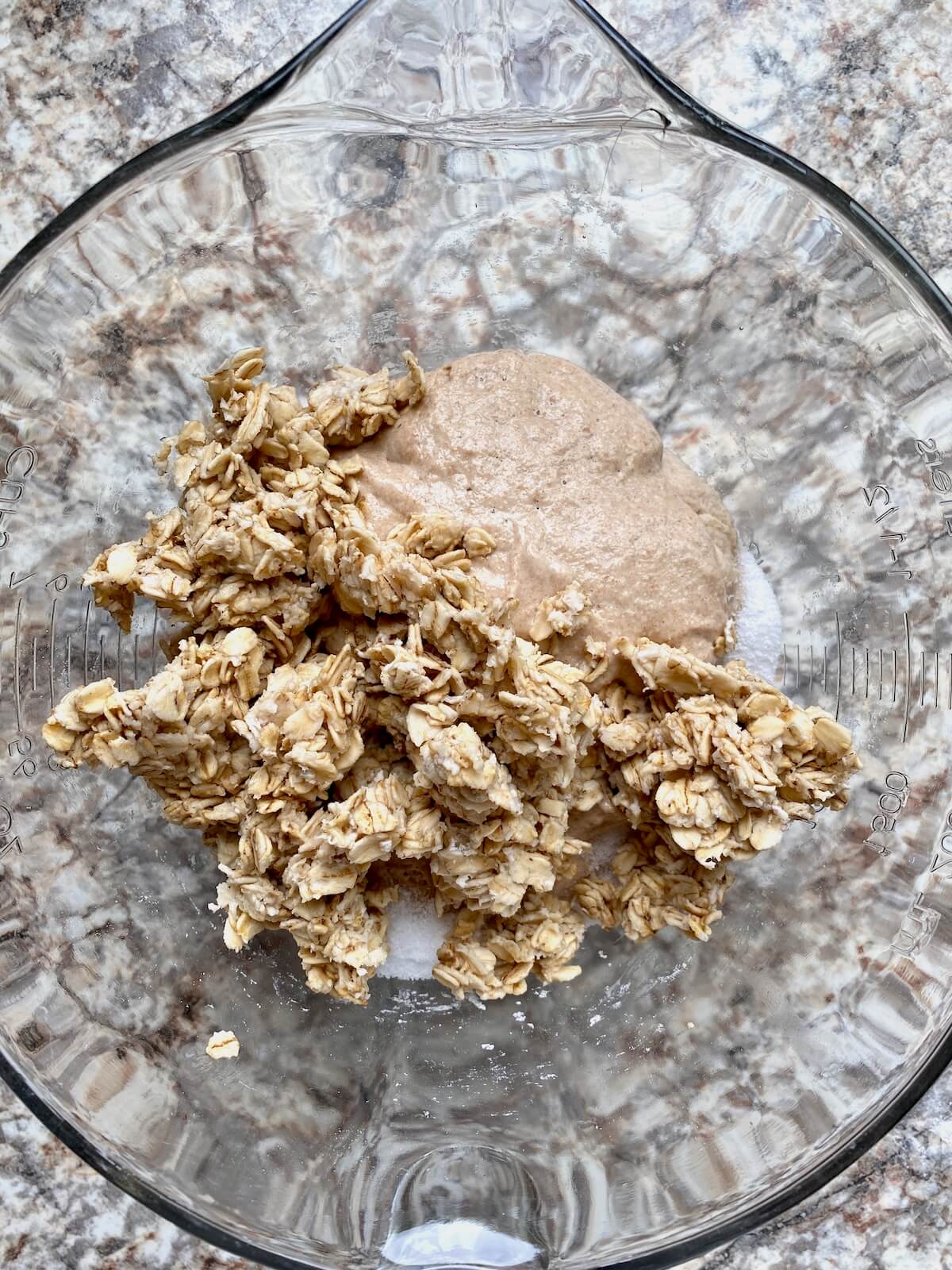 Soaked oats, sourdough starter, and salt on top of the autolysed flour and water in a glass bowl.