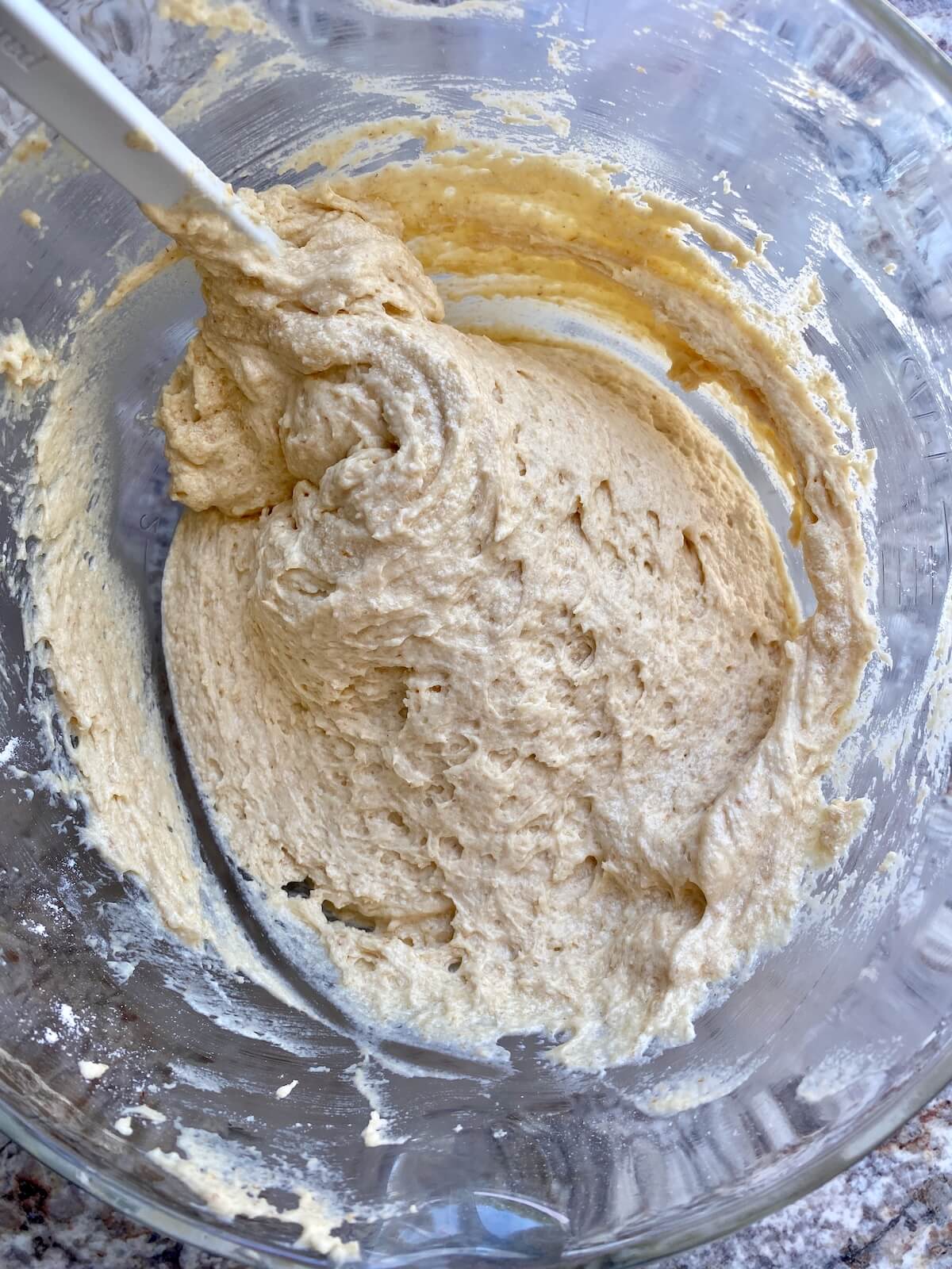 The cake batter mixed together in a glass bowl with a rubber spatula sticking out to the left.