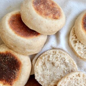 Several sourdough English muffins on a white cloth napkin. Two of the English muffins are cut in half.