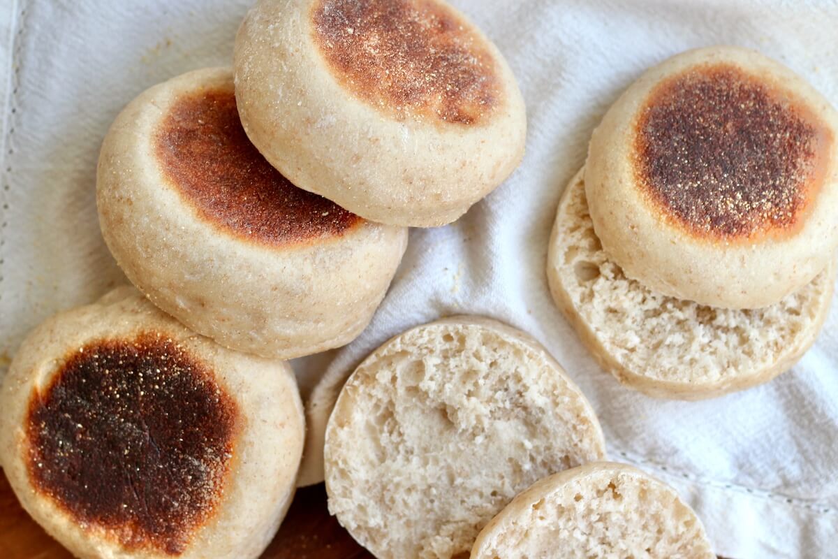 Several sourdough English muffins on a white cloth napkin. Two of the English muffins are cut in half.