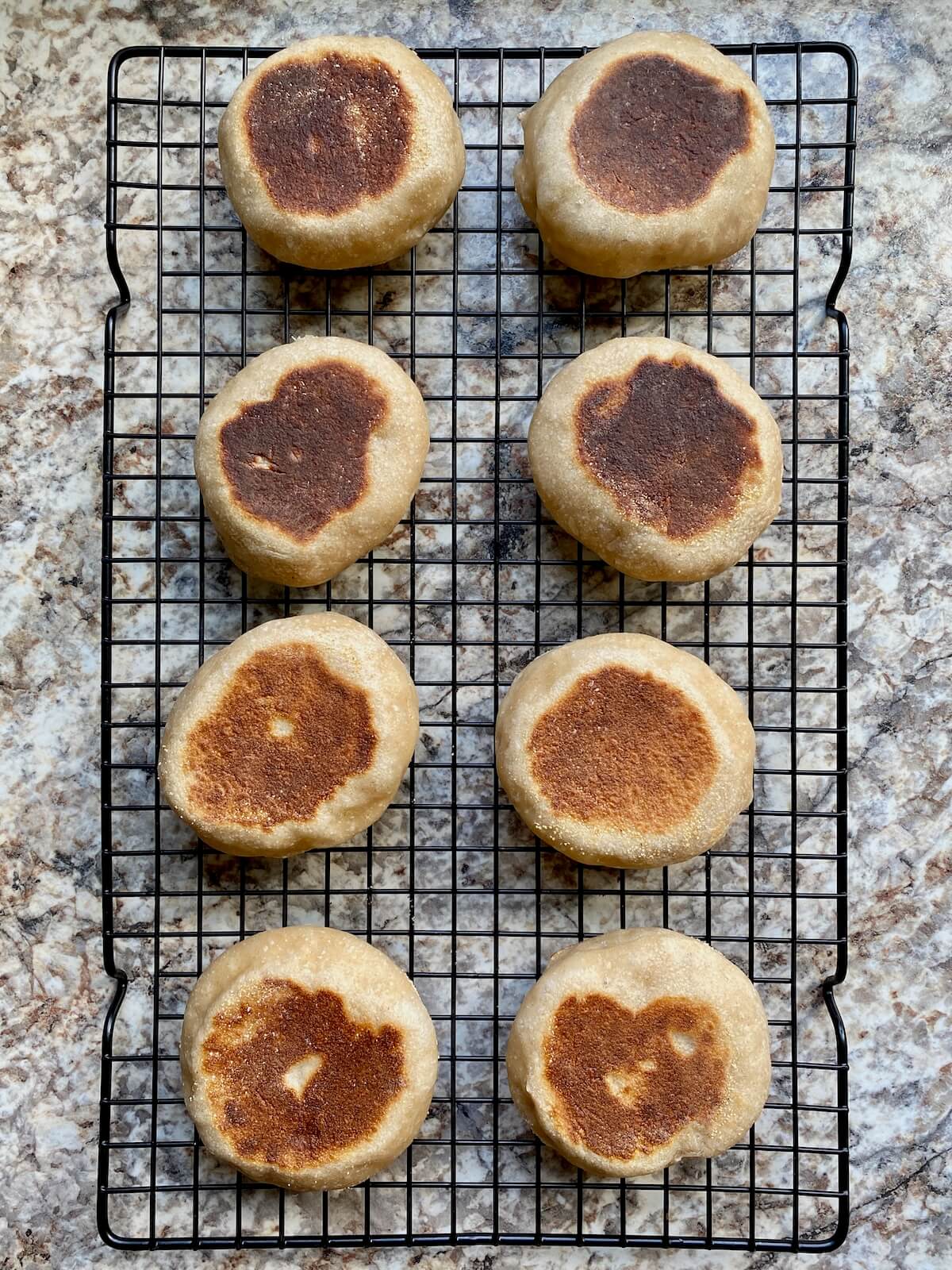 Eight sourdough English muffins on a wire cooling rack.