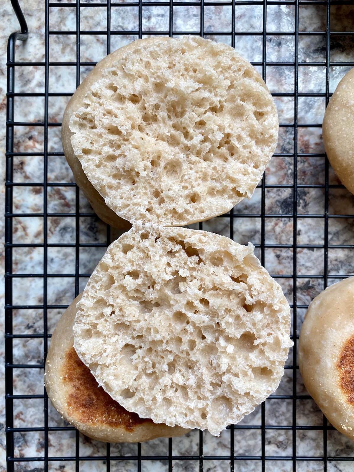 A fork-split sourdough English muffin on a wire cooling rack.
