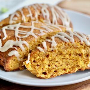 Three sourdough pumpkin scones drizzled with maple icing on a small white plate.