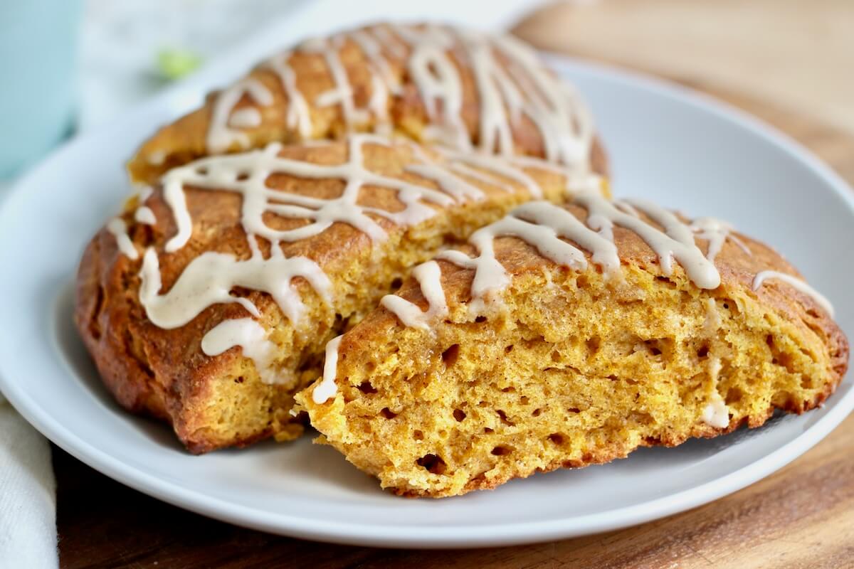 Three sourdough pumpkin scones drizzled with maple icing on a small white plate.