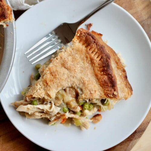 A slice of sourdough chicken pot pie on a small plate with a fork laying next to it.