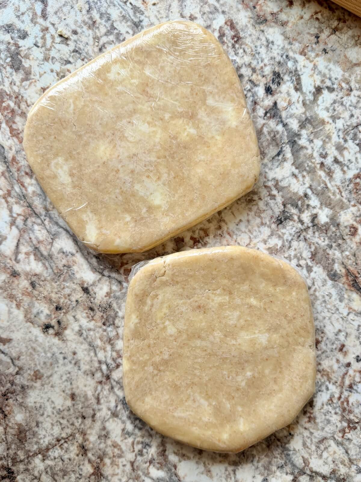 Two sourdough pie crusts wrapped in plastic wrap on a counter.