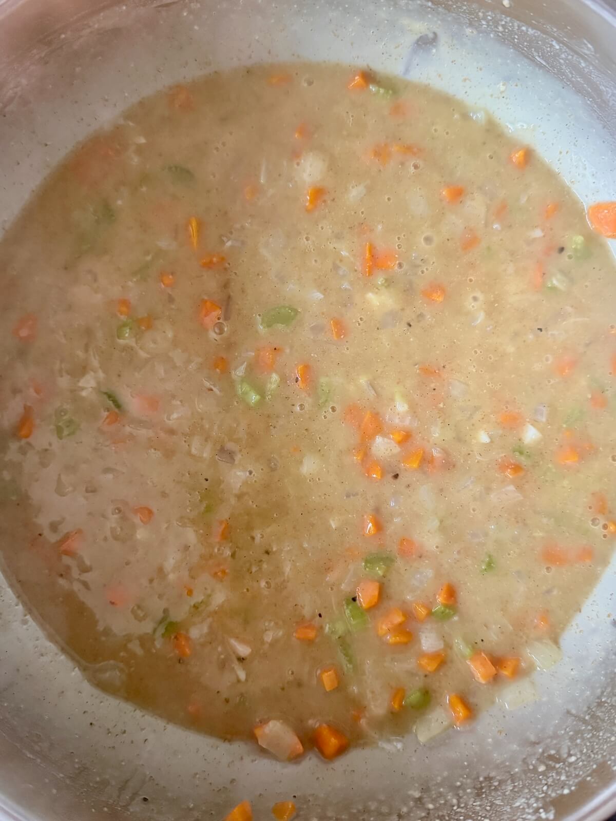 A mixture of thickened chicken stock and sautรฉed vegetables in a stainless steel pot.