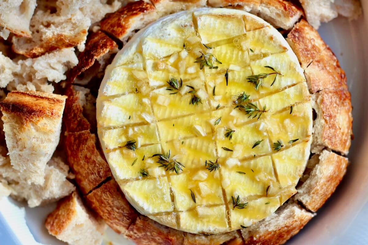 Baked brie in a sourdough bread bowl. The brie is topped with olive oil, honey, garlic, and thyme.