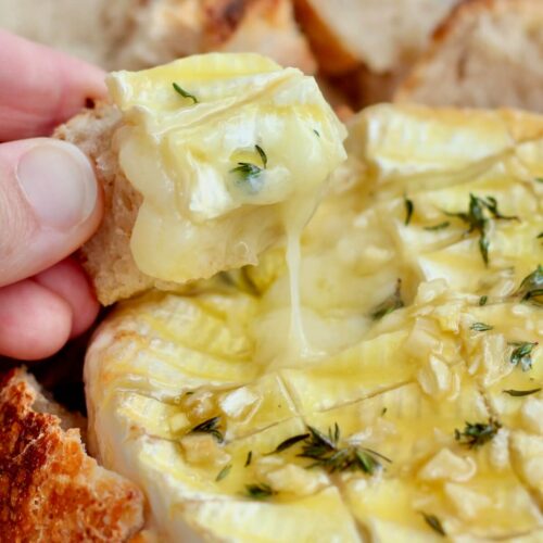 A hand scooping melty brie cheese up with a piece of sourdough bread.