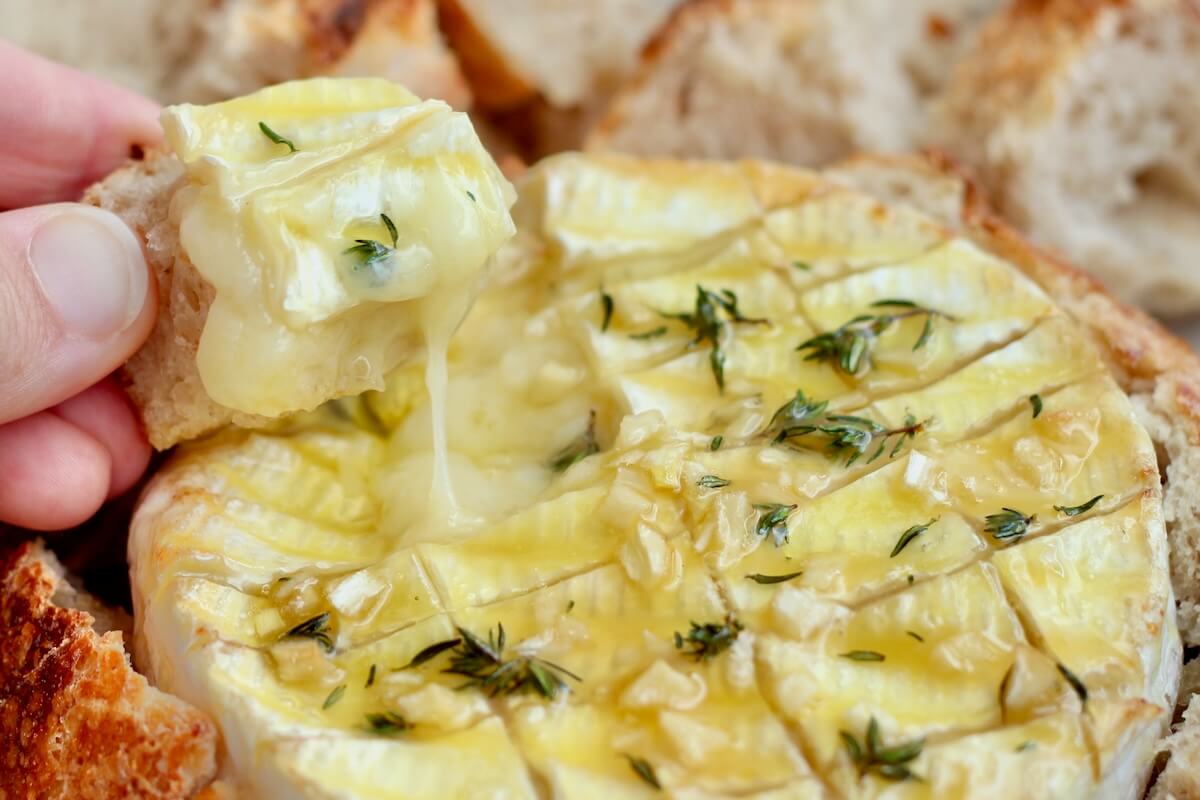 A hand scooping melty brie cheese up with a piece of sourdough bread.