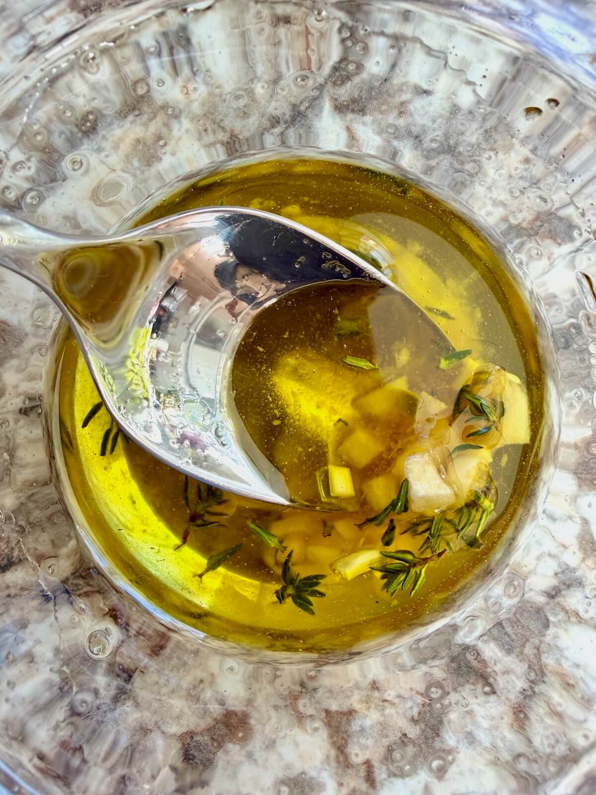 Olive oil, honey, garlic, and thyme mixed together in a small glass bowl with a metal spoon sticking out.