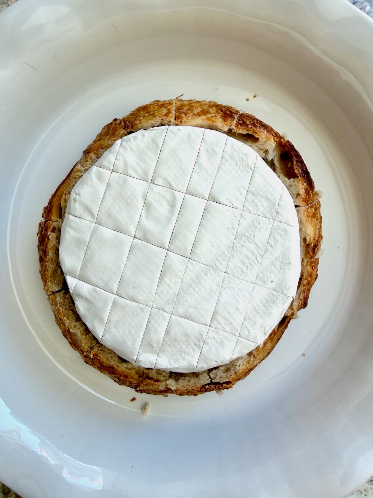 A scored wheel of brie cheese placed inside of a sourdough bread bowl.