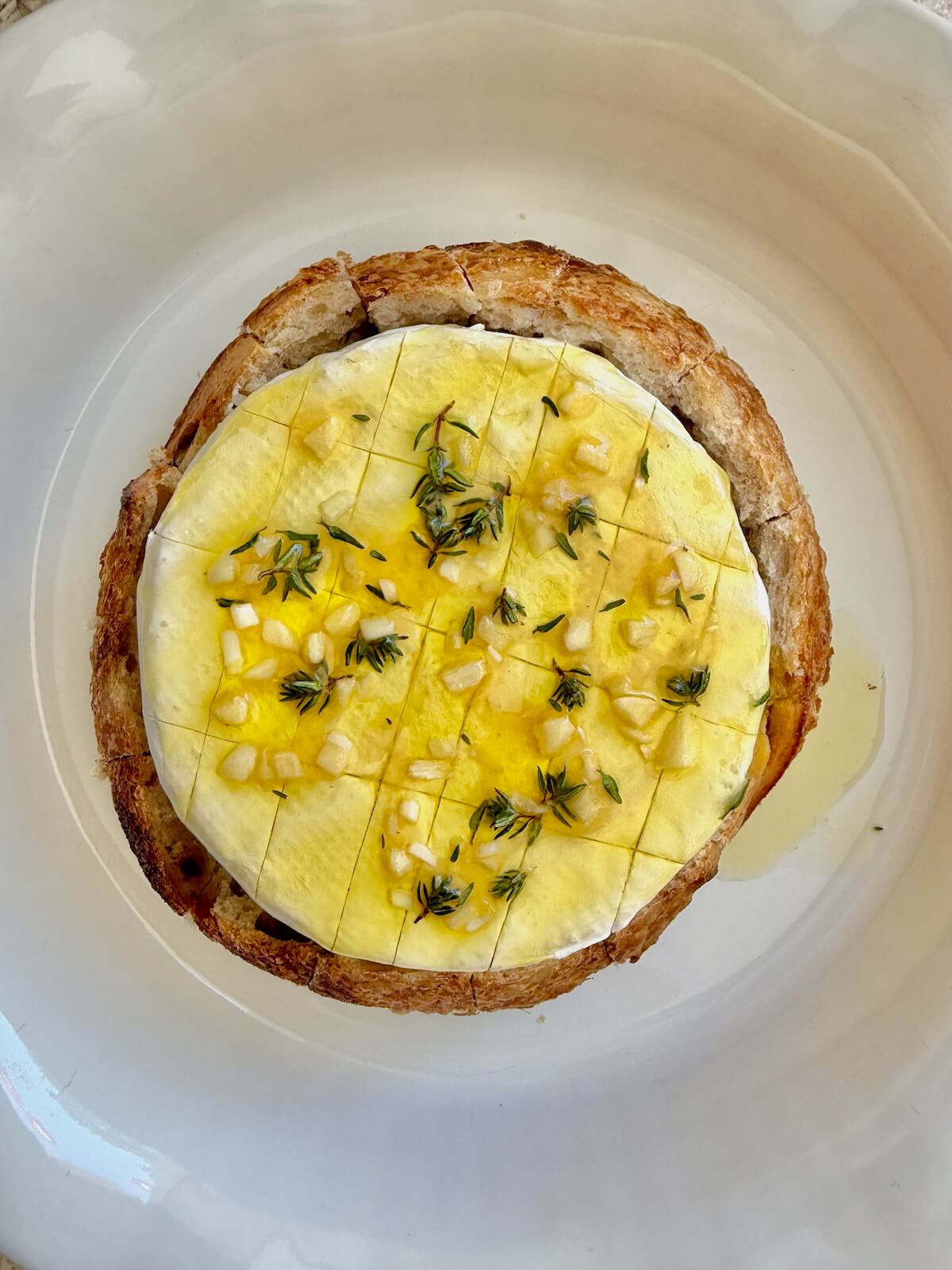 Brie cheese in a sourdough bread bowl topped with olive oil, honey, garlic, and thyme.