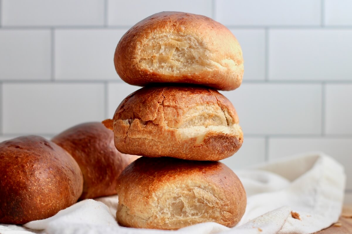 Three sourdough brioche buns stacked on top of each other. There are two more buns out of focus in the background.