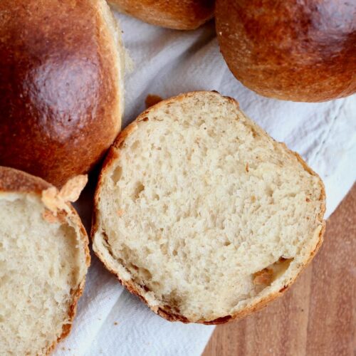 Sourdough brioche buns on a linen cloth. One of the buns is sliced in half to show the soft texture.