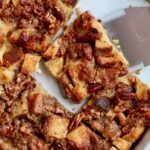A baking dish of sourdough french toast casserole with a few pieces missing and a spatula removing a piece.