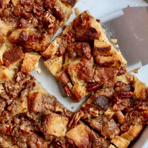 A baking dish of sourdough french toast casserole with a few pieces missing and a spatula removing a piece.