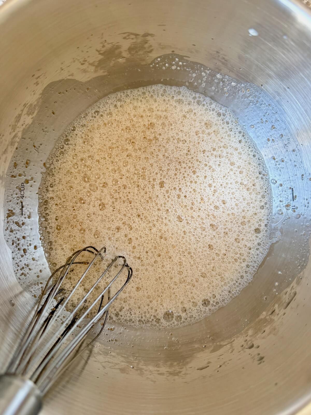Sourdough starter, honey, and water whisked together in a stainless steel bowl.