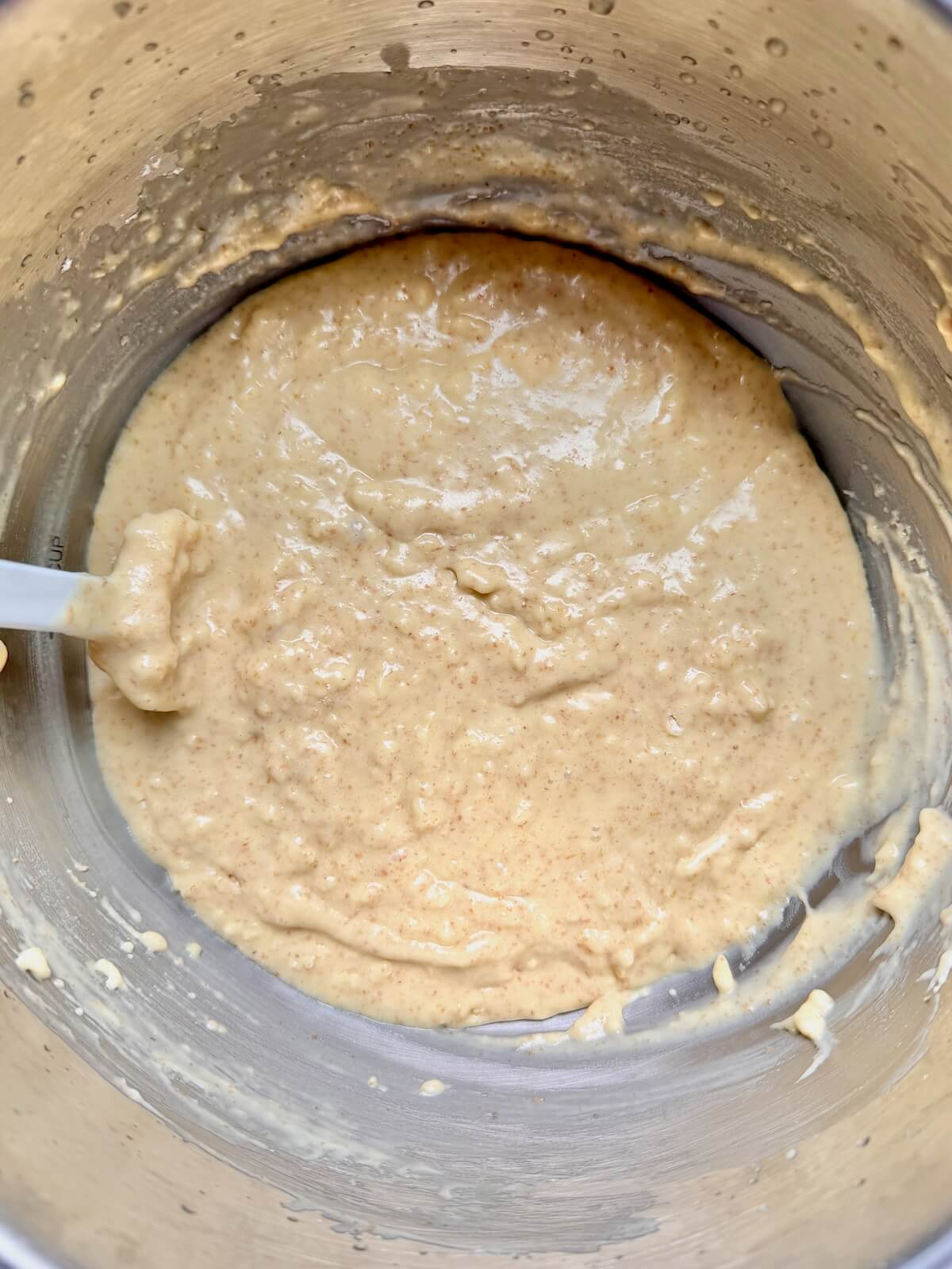 The wet and dry ingredients mixed together with a white rubber spatula in a stainless steel mixing bowl.