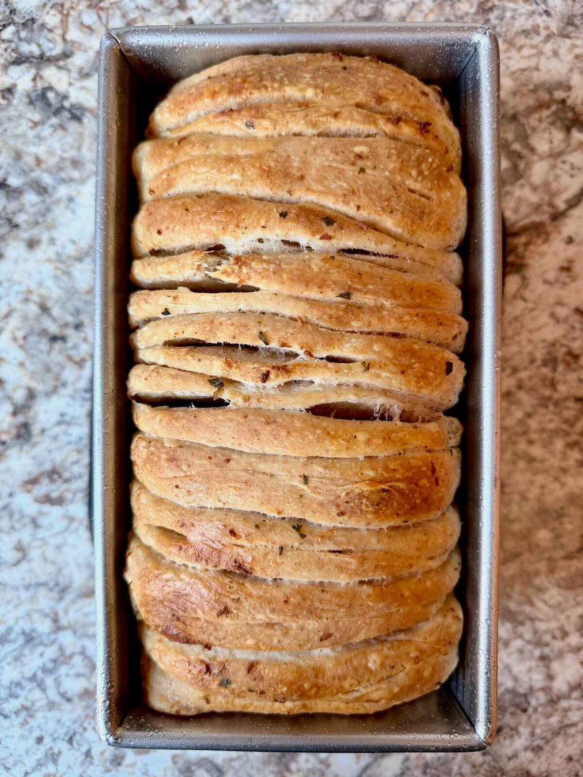 A baked loaf of sourdough pull apart garlic bread in a loaf pan.